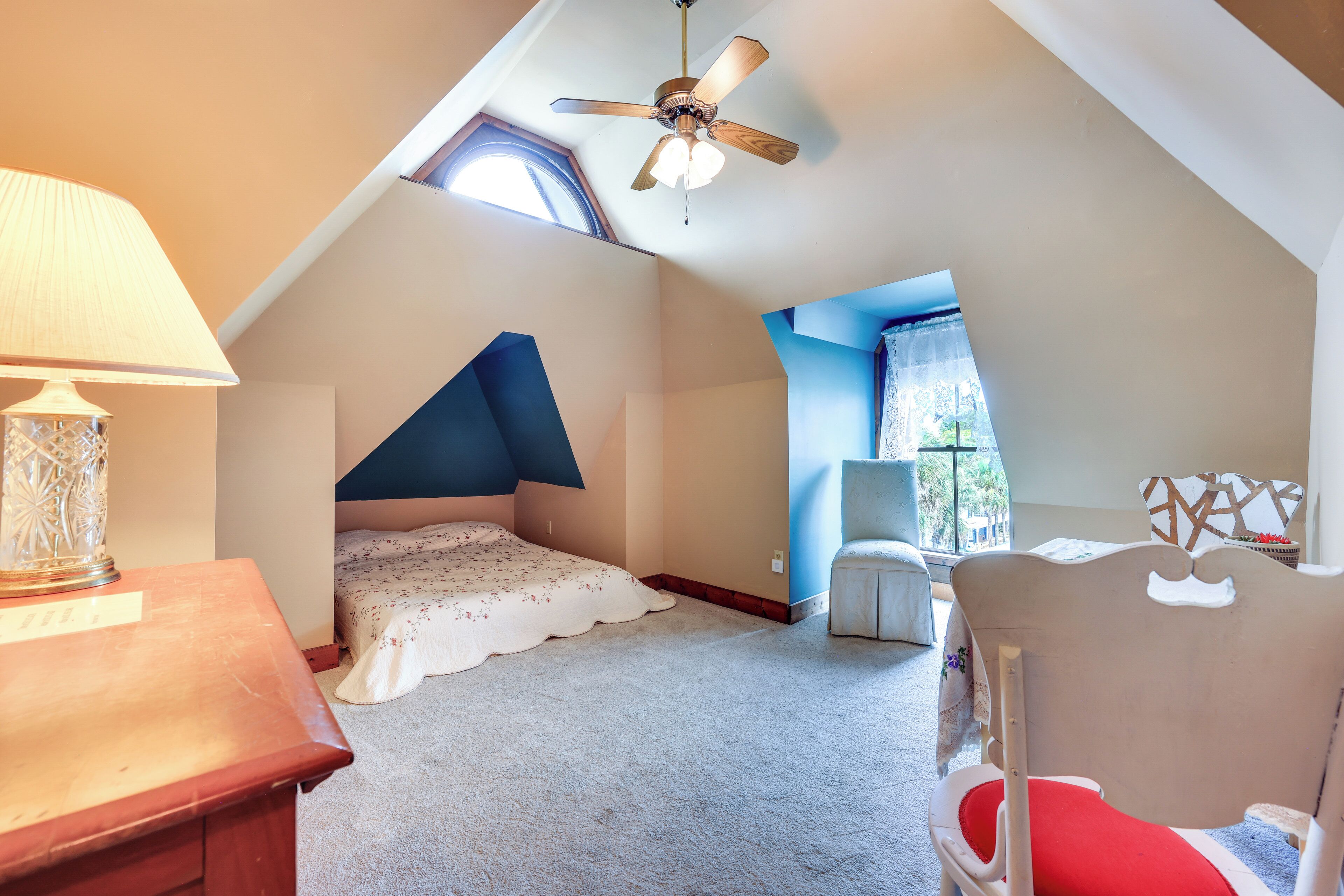 A bedroom with a sloped ceiling, a bed, a chair, a lamp, and a window.