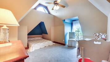 Une chambre avec un plafond en pente, un lit, une chaise, une lampe et une fenêtre.