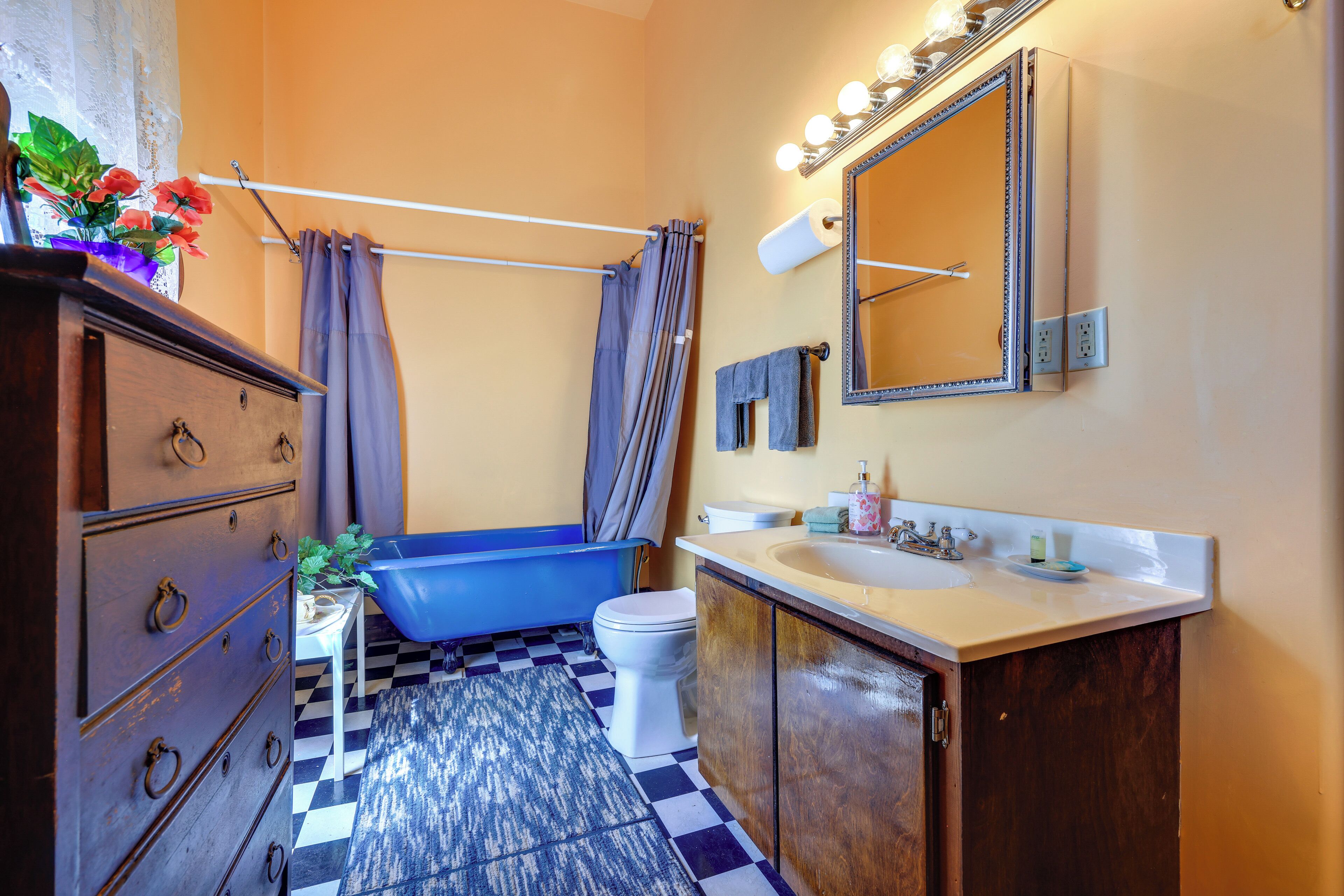 A bathroom with a blue bathtub, a white toilet, a wooden cabinet, and a sink with a mirror above it.