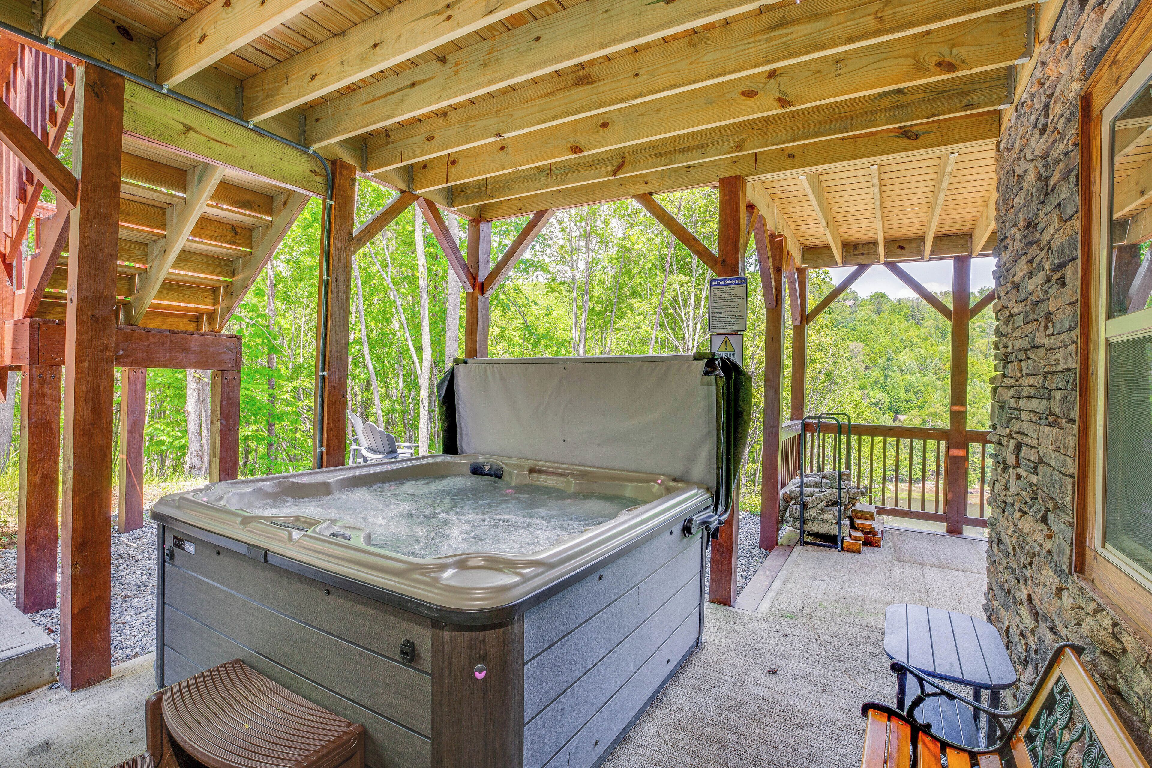 Un bain à remous sous une pergola en bois aux murs en pierre, entouré d’une terrasse et de bancs.