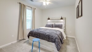Ein Schlafzimmer mit Bett, Deckenventilator, Fenster mit Vorhängen und einem kleinen Hocker.