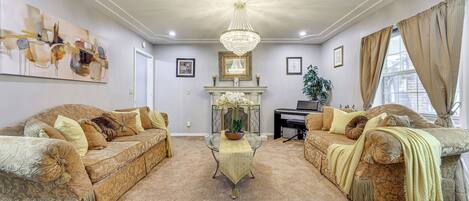 A living room with two sofas, a chandelier, a fireplace, and framed artwork on the walls.