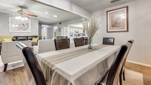 Un coin repas avec une table dressée pour six personnes, entourée de fauteuils en cuir, un vase rempli de fleurs et des œuvres d’art encadrées accrochées aux murs.