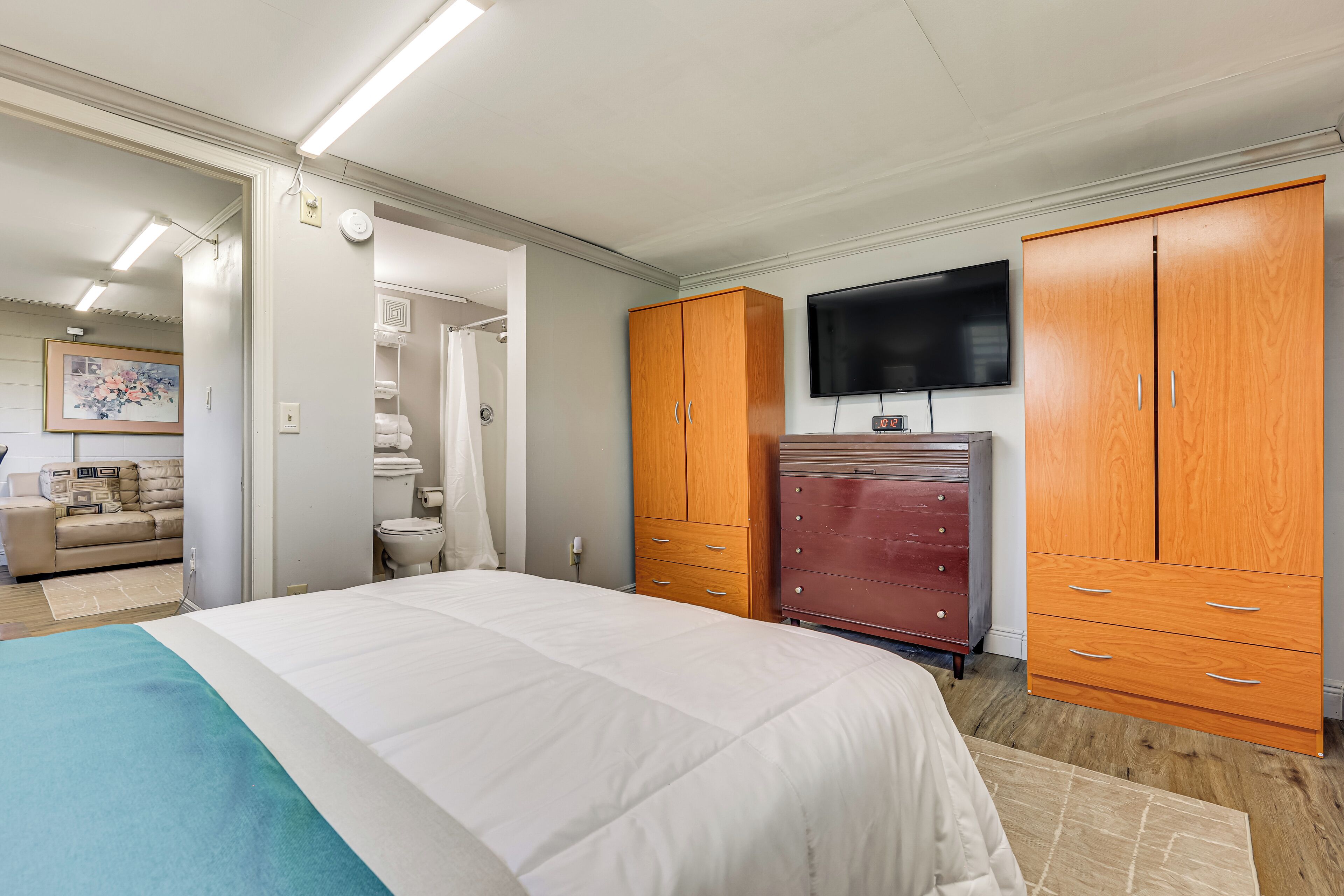 A bedroom with a bed, wooden wardrobe, a television, and a bathroom visible through an open door.