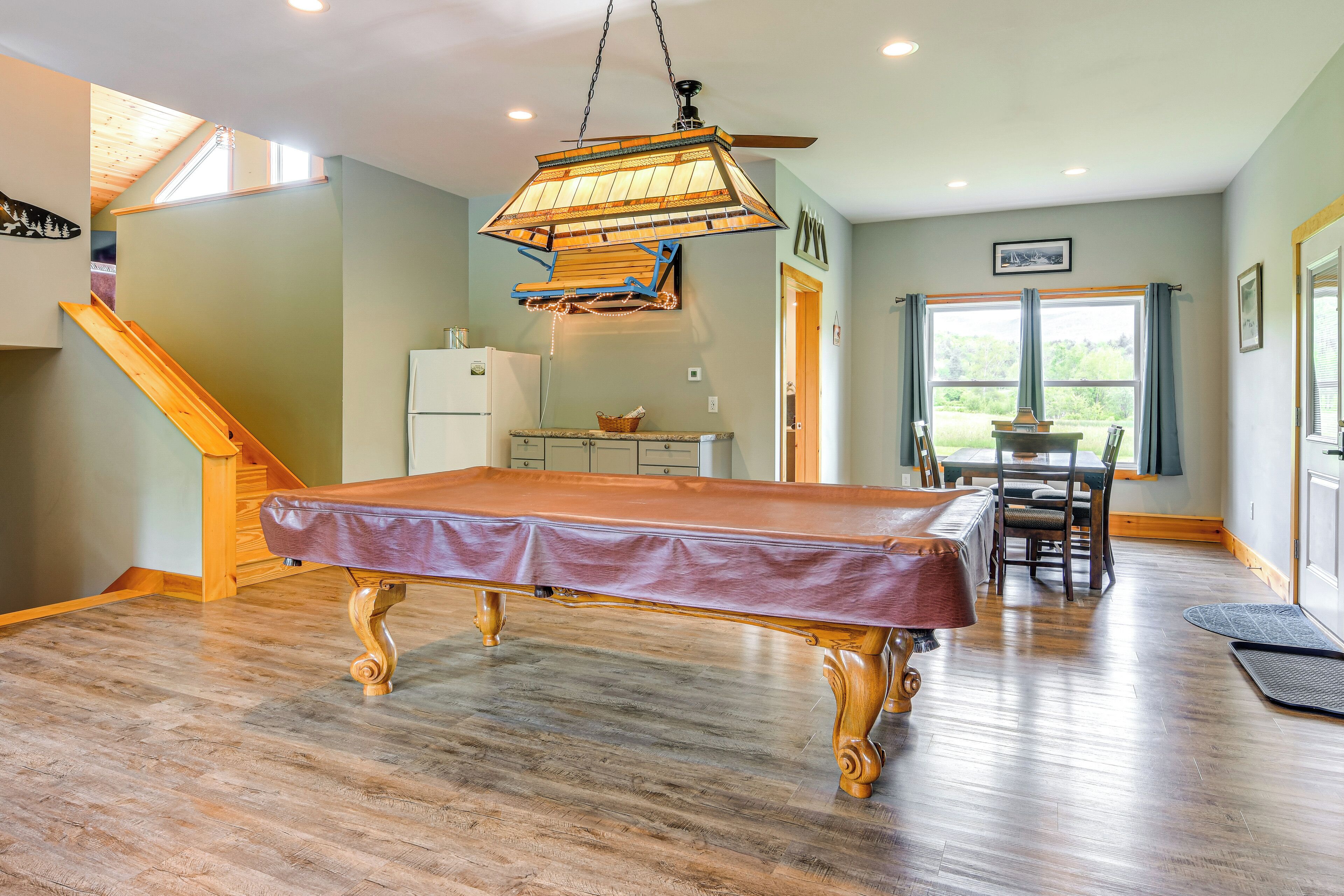 A pool table in a room with a wooden floor, a ceiling fan, and a dining area with a table and chairs.