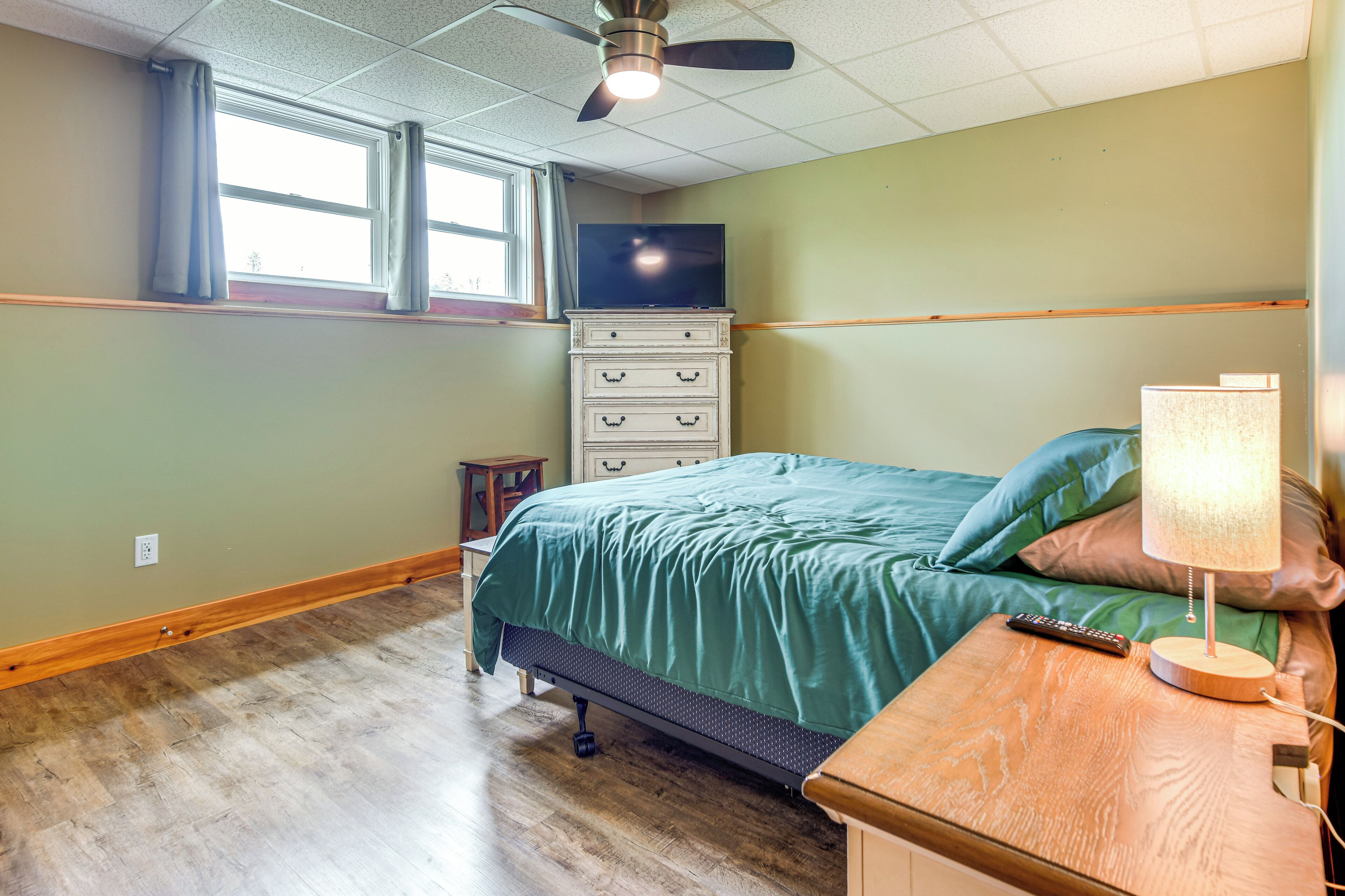 A bedroom with a bed, a nightstand, a TV on a dresser, and a ceiling fan.