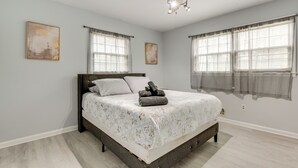 Une chambre à coucher avec un lit, un ventilateur de plafond et deux fenêtres avec des rideaux.