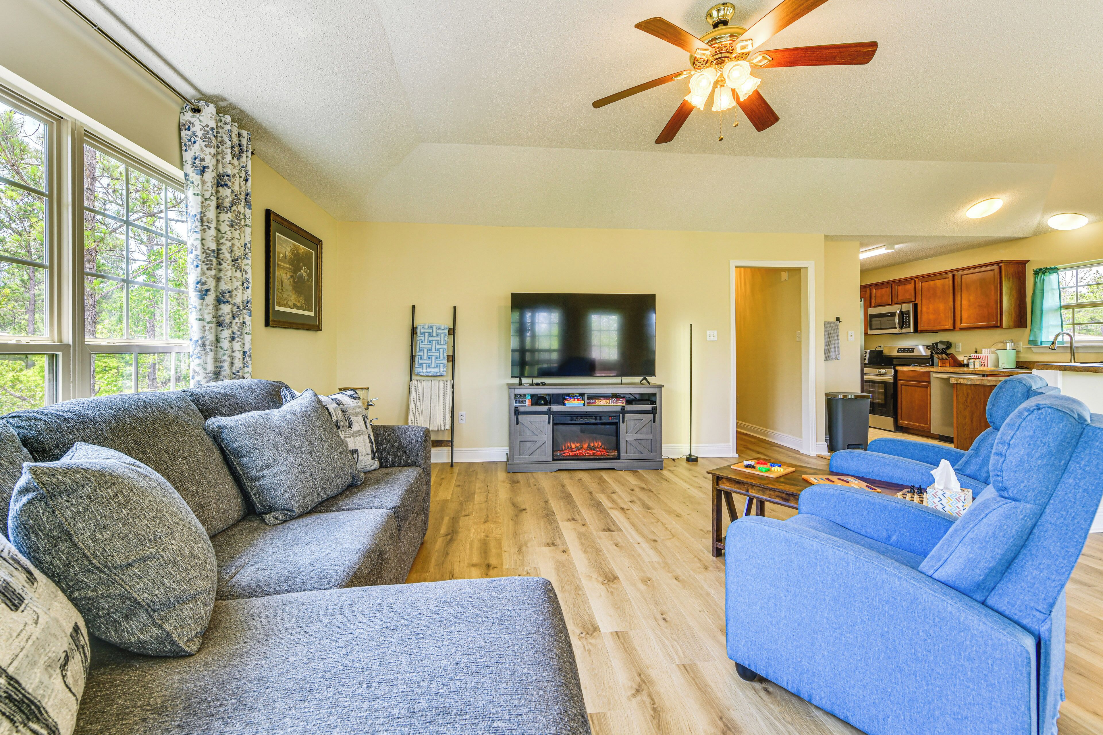 A living room with a gray sofa, blue armchair, wooden flooring, and a ceiling fan.
