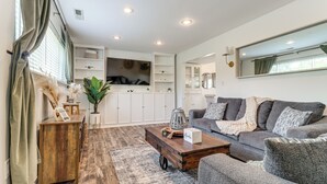 Ein modernes Wohnzimmer mit einem grauen Sofa, einem Holztisch und einem großen Fernseher.