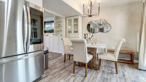 Eine moderne Küche mit einem Edelstahlkühlschrank, weißen Schränken und einem Essbereich mit Holztisch und -stühlen.