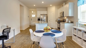 A modern kitchen with white cabinets, a refrigerator, and a microwave. There is a dining table with chairs and a fruit bowl. - 3 Mi to Dtwn Kyle: Wfh-friendly Home w/ Patio (Kyle)