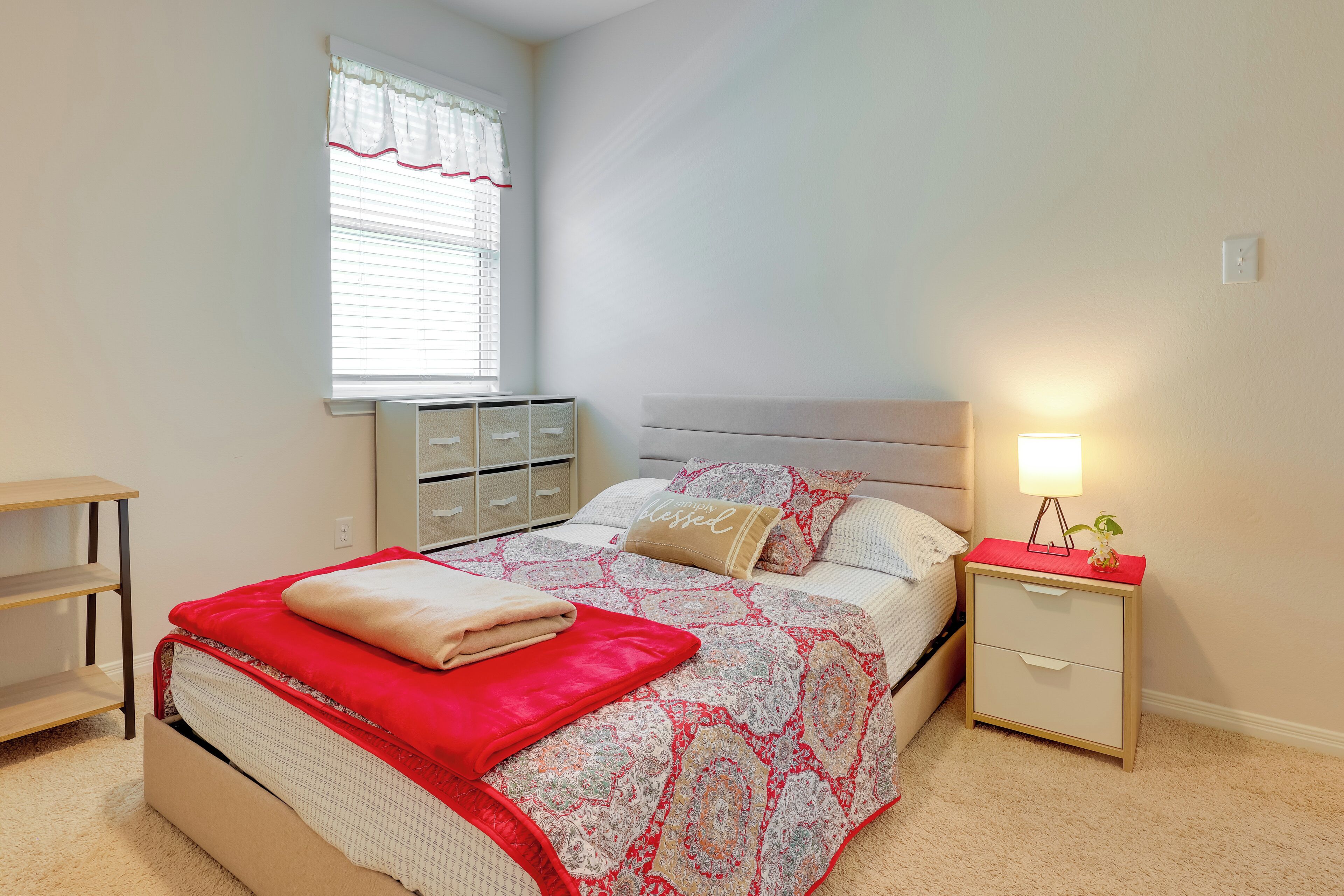 Une chambre à coucher bien rangée, avec un lit, des tables de chevet, une commode et une fenêtre équipée de stores.