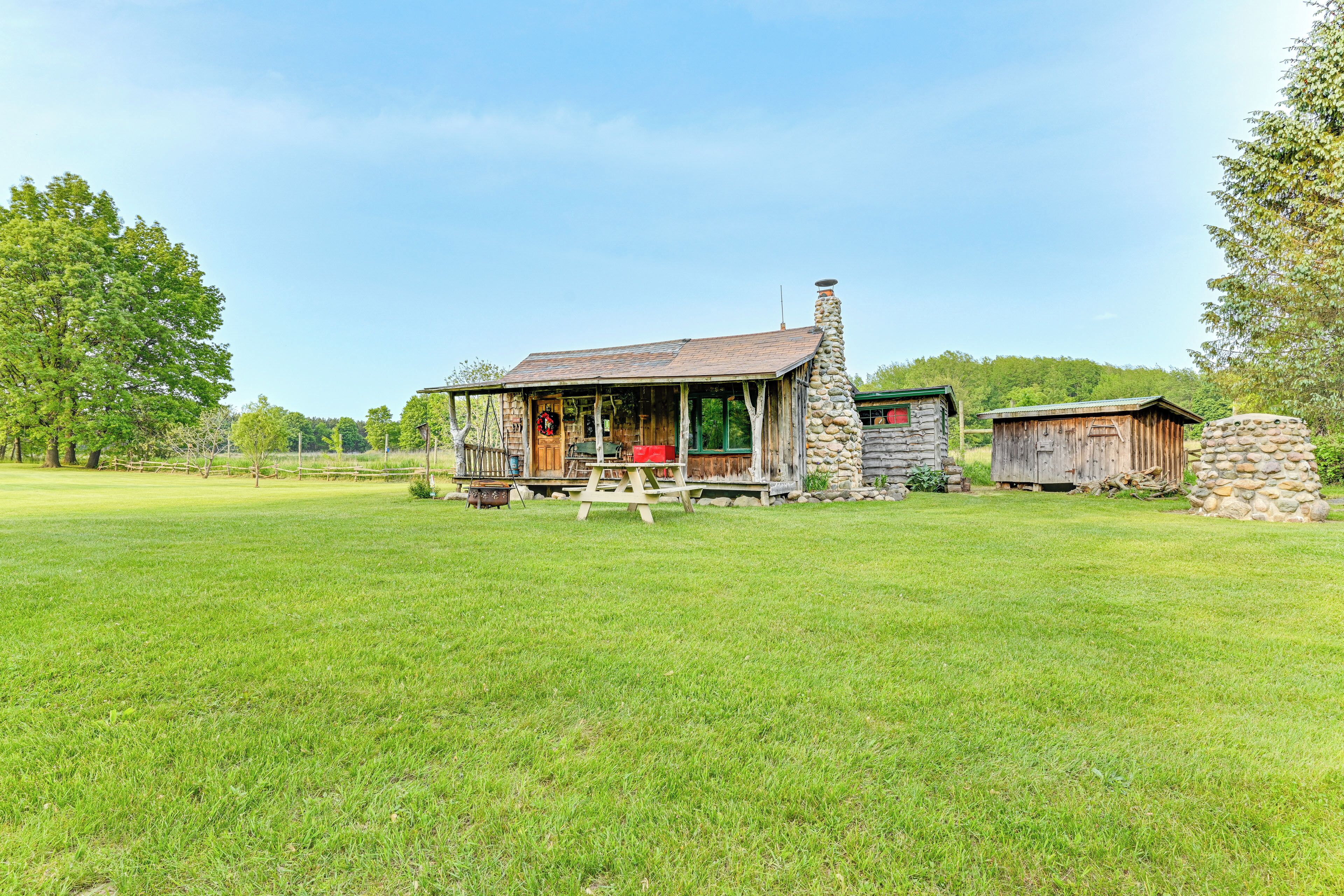 Une cabane rustique avec une cheminée en pierre, une terrasse en bois et une table de pique-nique, le tout situé dans un champ verdoyant.