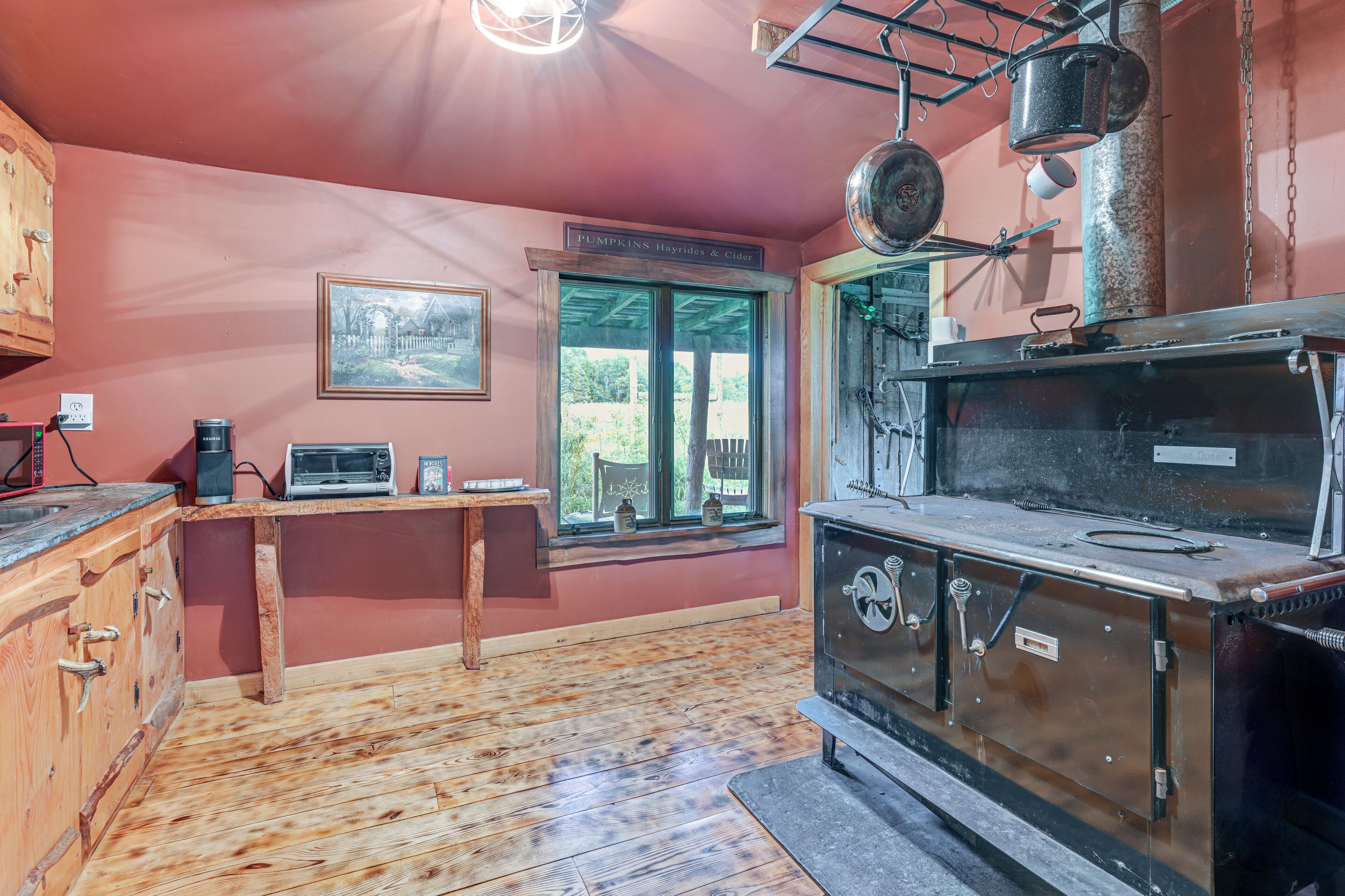 A rustic kitchen with a wood stove, a window with a view, and a sign indicating pumpkin harvest.
