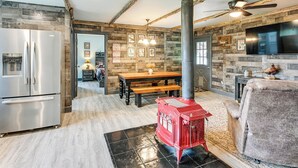 A modern kitchen with a stainless steel refrigerator, a red wood-burning stove, and a dining area with a wooden table and benches. - 5-acre Kingston Getaway: Sauna & Fire Pit (Kingston)