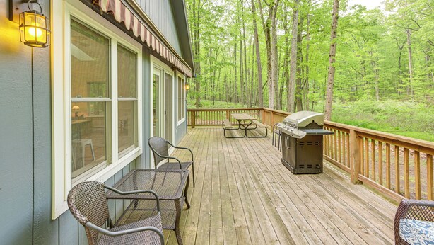 Une terrasse en bois avec des sièges d’extérieur, un barbecue et une vue sur une zone boisée.