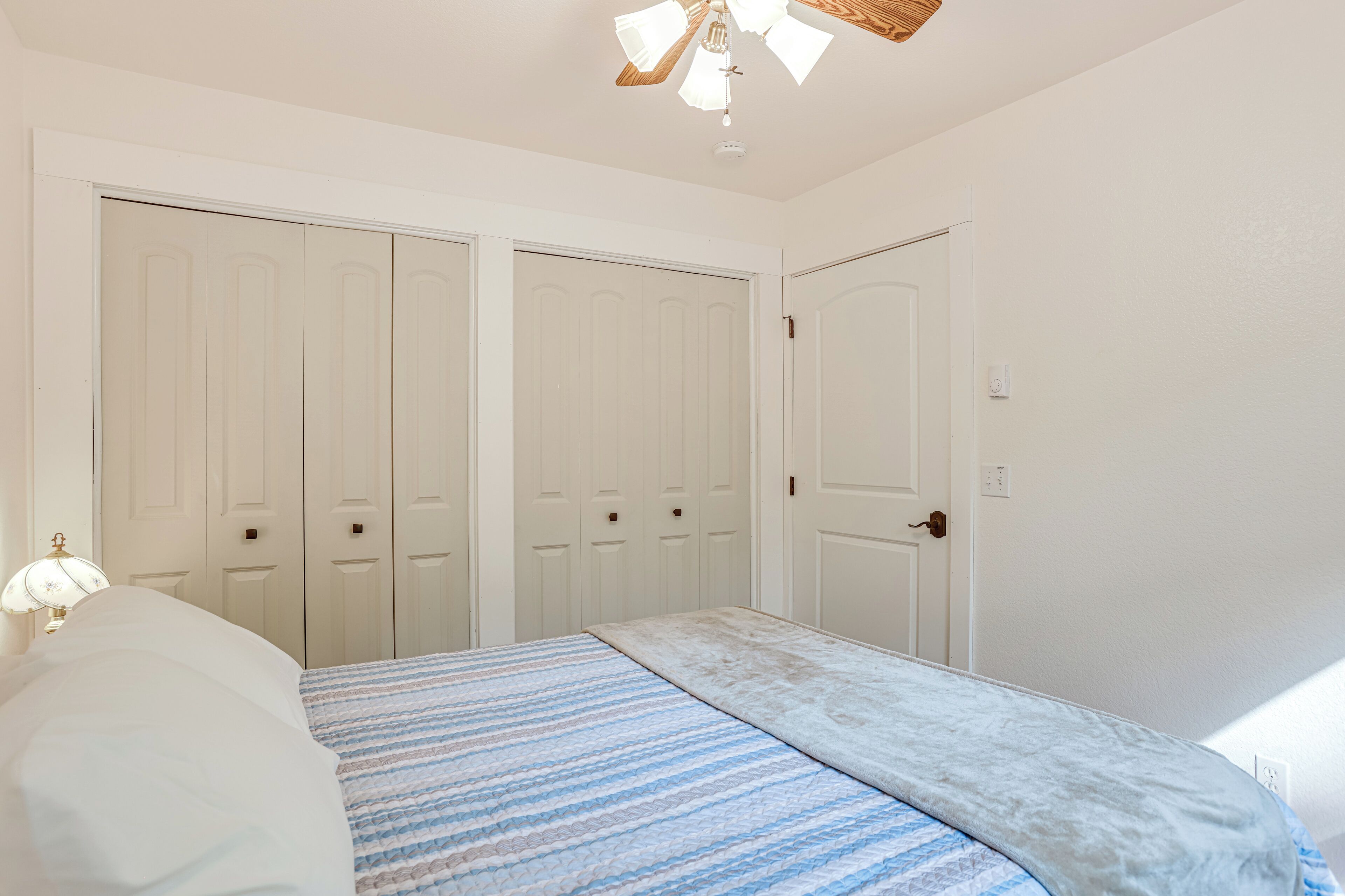 A bedroom with a bed, a ceiling fan, and white wardrobes.