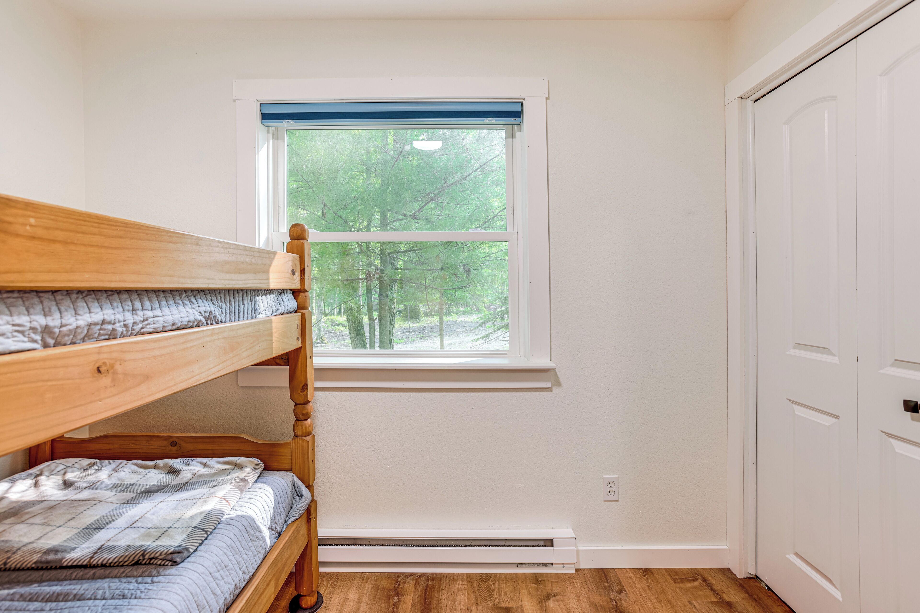 A room with a bunk bed, a window with a view of trees, and a white wardrobe.