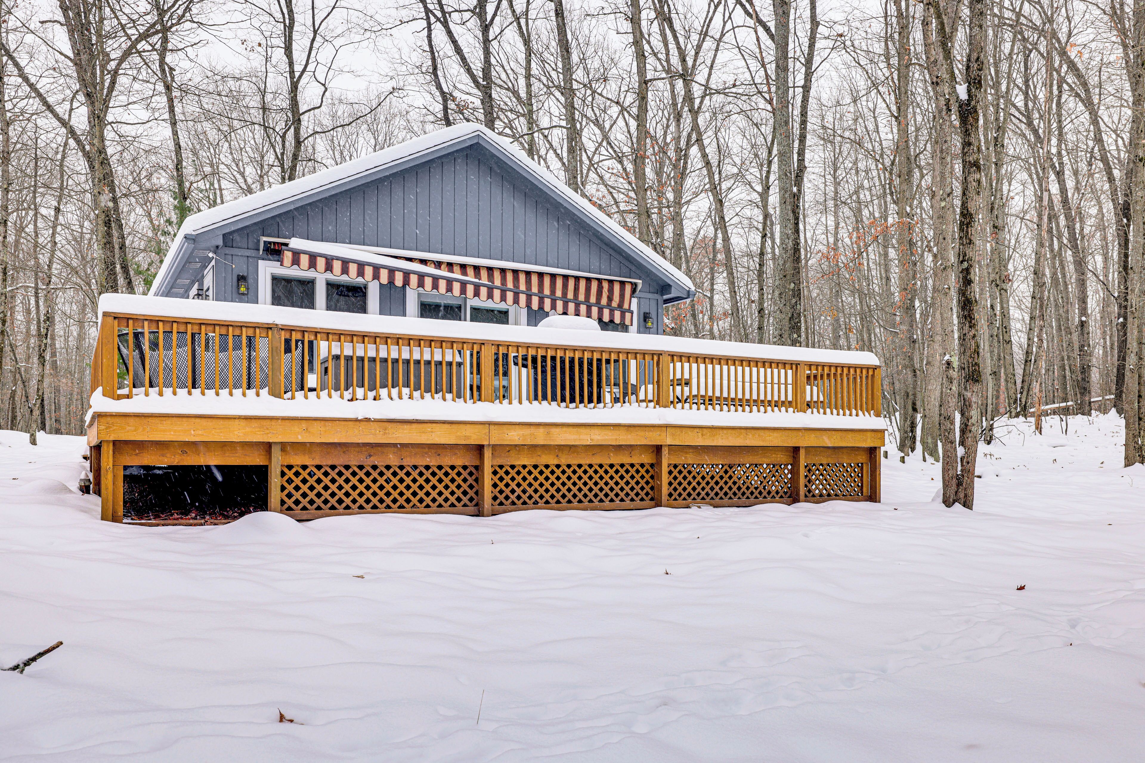 Uma cabana com deck de madeira e varanda coberta, rodeada por uma floresta nevada.
