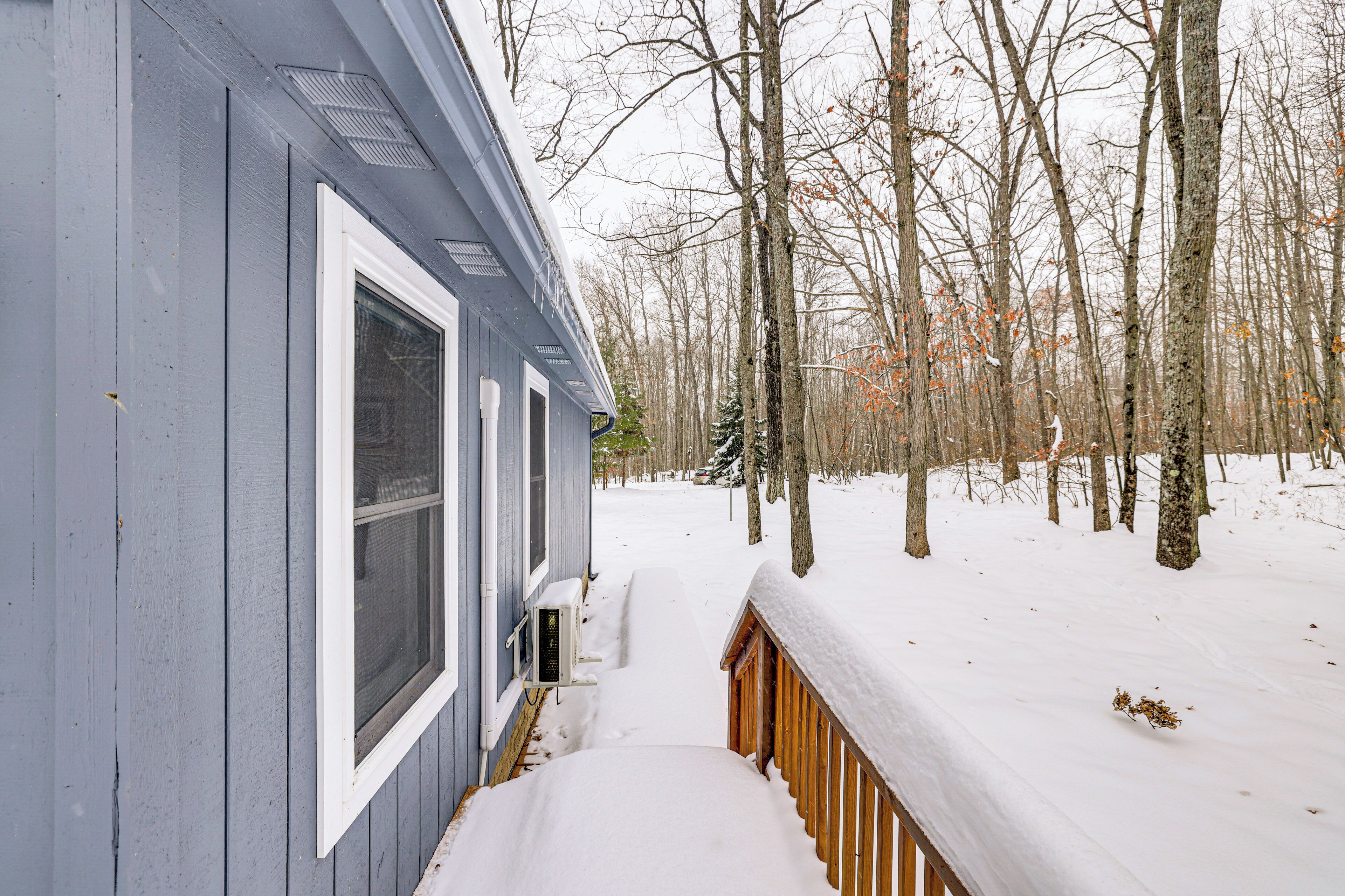 A snow-covered wooden deck leading to a house with a blue exterior and white trim.