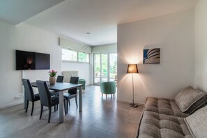 A modern living room with a dining area, a sofa, a floor lamp, and a painting on the wall. - Stylish 2-Bedroom Apartment by Lake Como (Como)