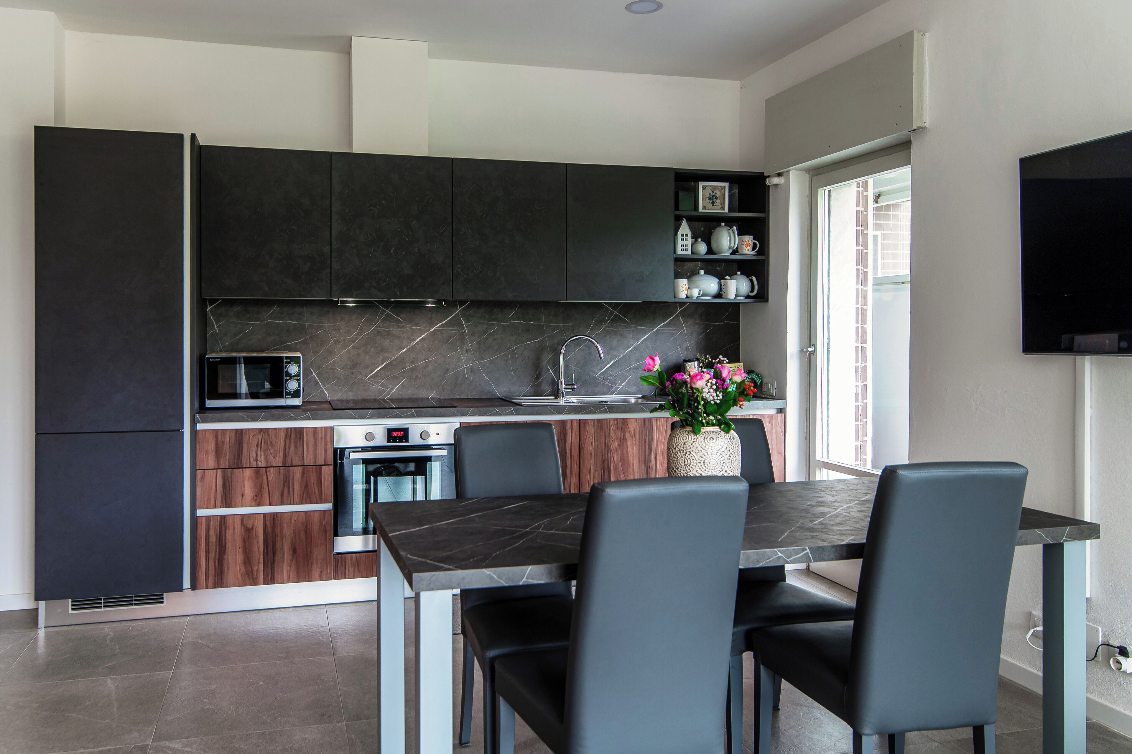 A modern kitchen with dark cabinetry, a built-in microwave, and a dining area with a table and chairs.