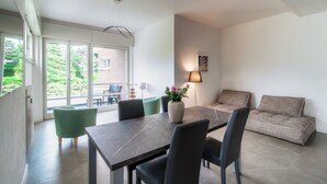 A modern dining area with a dark marble table, black chairs, and a vase of flowers. There is a green armchair and a beige sofa in the background.