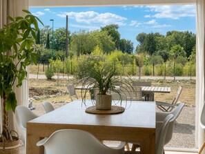 A dining area with a wooden table and white chairs, a potted plant, and a view of a landscaped garden with trees and shrubs. - Lorgues: 3-BR house, private pool, A/C & fiber Wi-Fi (Lorgues)
