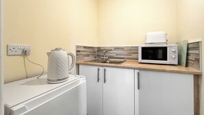 A compact kitchen with a microwave, kettle, and a sink.