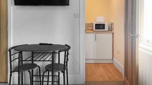 A room with a dining table and chairs, a flat-screen TV mounted on the wall, a microwave on a counter, and a door leading to another room.