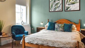 A bedroom with a large bed, a blue chair, a wooden headboard, and two framed leaf paintings on the wall.