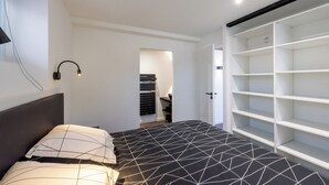 Ein modernes Schlafzimmer mit einem Bett, einem Kopfteil, einer Wandleuchte und einem Einbauschrank.