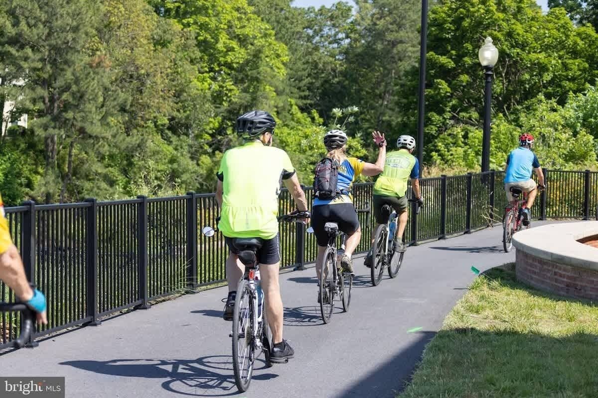 A paved pathway with cyclists, surrounded by greenery and a black metal fence.