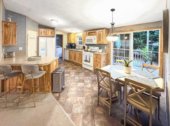 Una cocina con armarios de madera, una zona de comedor con mesa y sillas, un refrigerador, un microondas y una estufa.