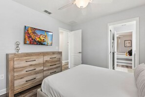 Un dormitorio con cama, cómoda, ventilador de techo y una puerta que da a otra habitación.