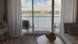 A living room with a view of a river, a balcony with a chair, and a sofa.