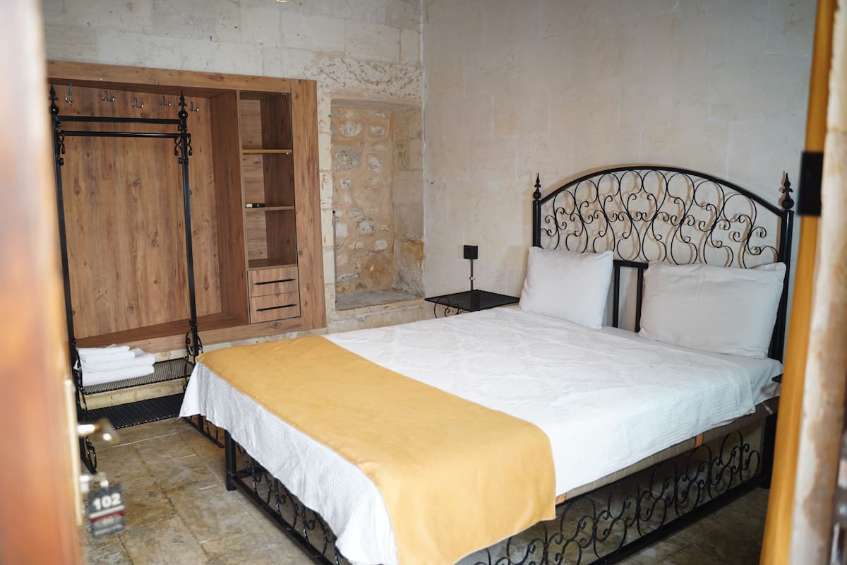 Un dormitorio con cama, armario de madera, pared de piedra y una mesita.