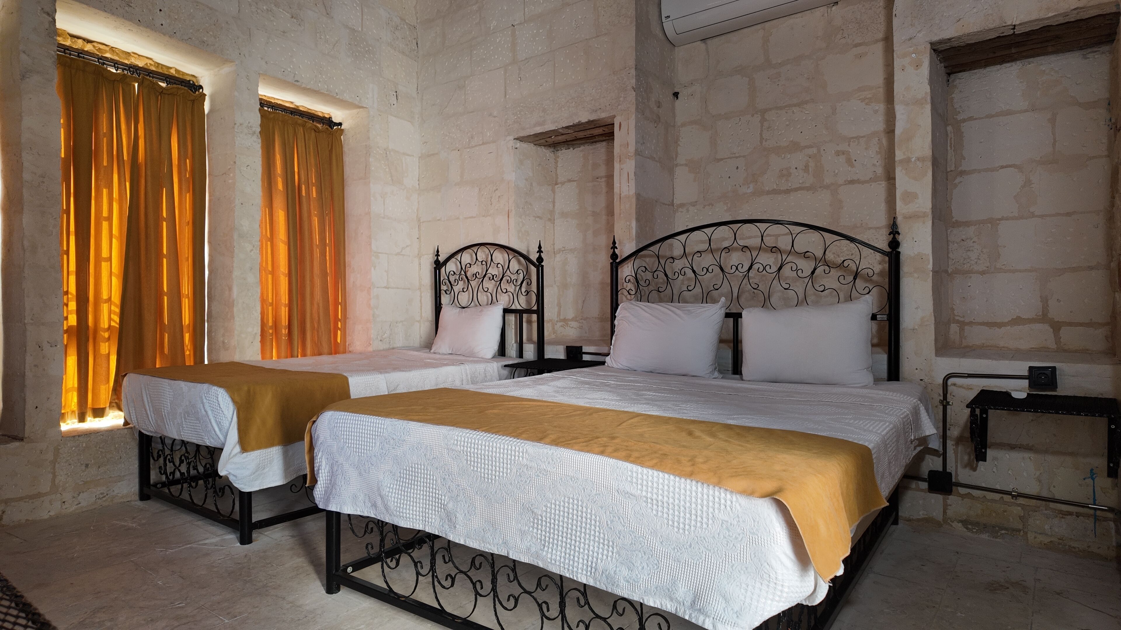 A room with two beds, a window with curtains, and a stone wall.