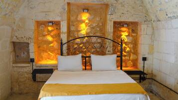 Una habitación con paredes de piedra, una cama, dos mesitas de noche y dos lámparas de pared.