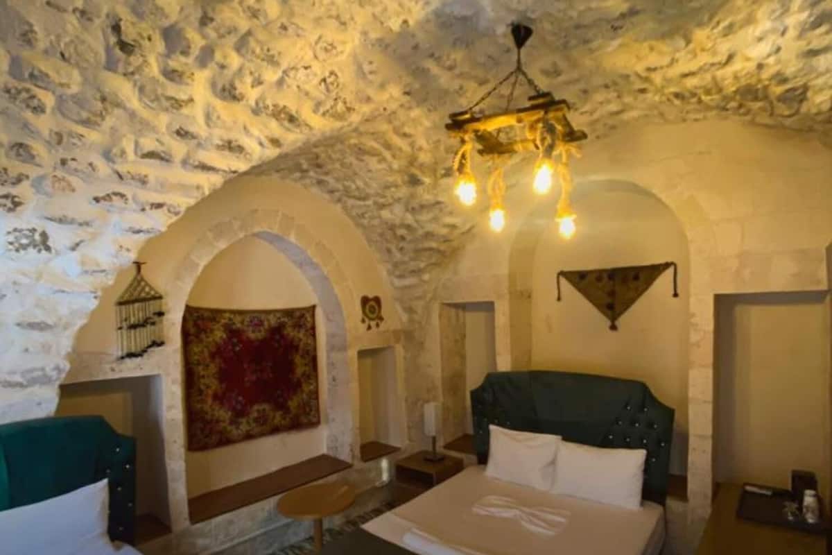Una habitación con techo de piedra, una cama con cabecera verde, una mesita y una araña.