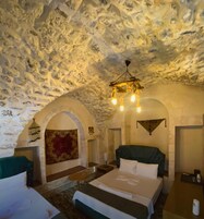 Una habitación con techo de piedra, una cama con cabecera verde, una mesita y una araña.