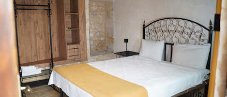 A bedroom with a bed, wooden wardrobe, and a stone wall.
