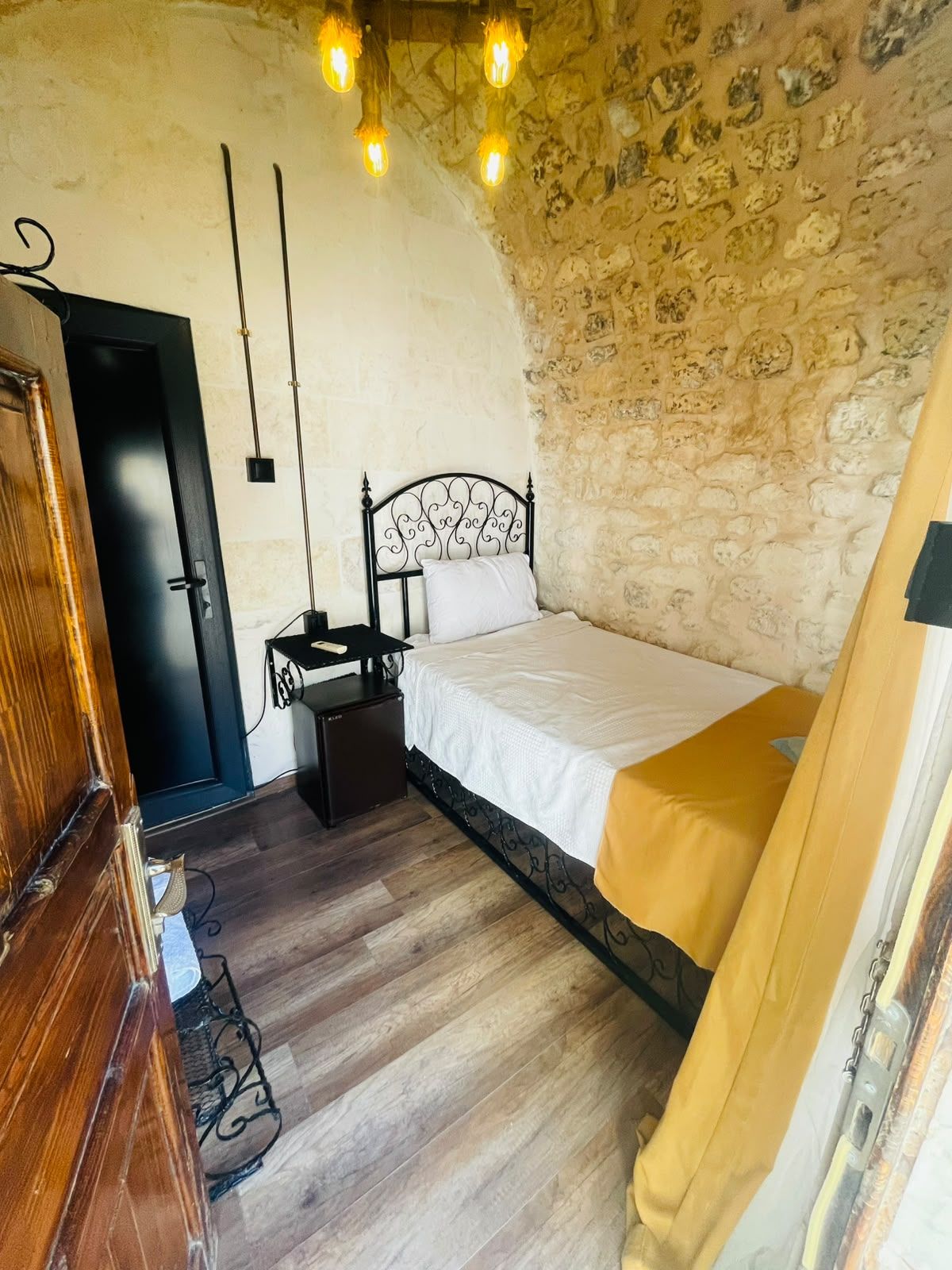 Un dormitorio con pared de piedra, cama con sábana blanca, cómoda de madera y escritorio con silla.