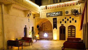 Une auberge traditionnelle dont l’enseigne porte l’inscription « HIZMALI ». Elle se distingue par son portail en arc de cercle, un escalier menant à un étage supérieur et un espace détente avec des bancs.
