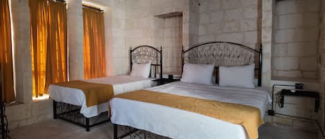 A room with two beds, a window with curtains, a wall-mounted air conditioner, and a metal table.