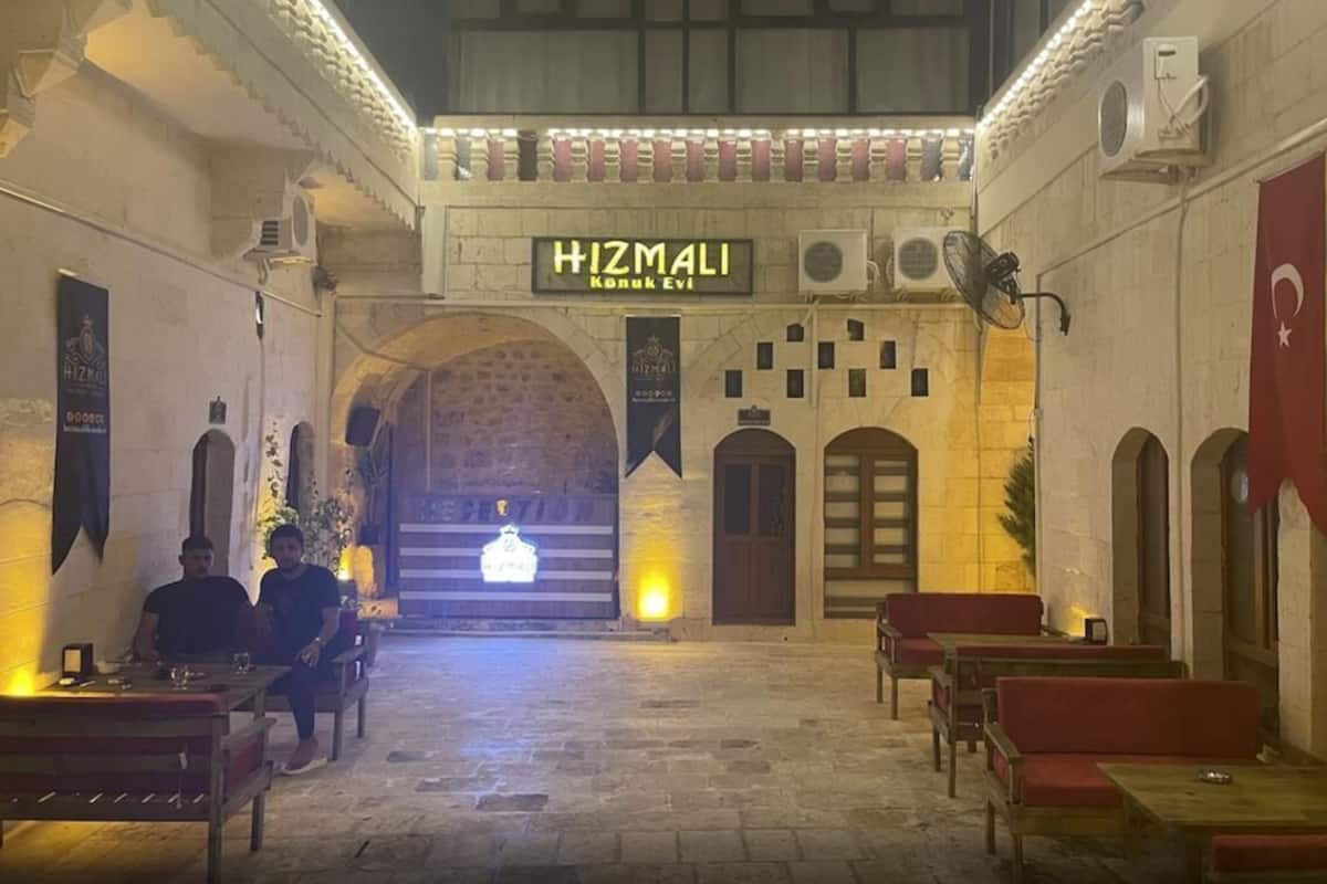 Un interior tradicional con un arco central, bancos y un letrero que dice "HIZMALI Konuk Evi".