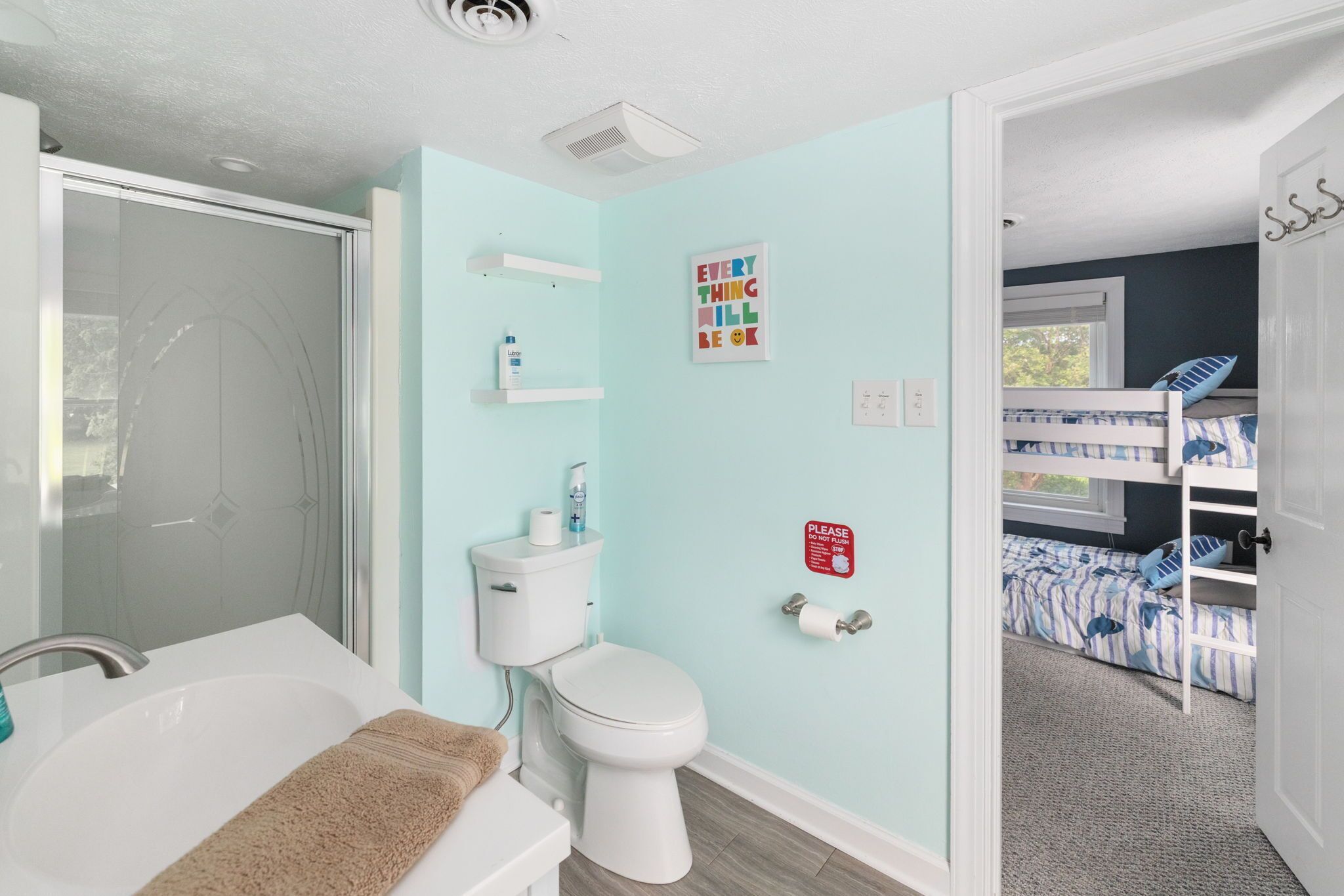 A bathroom with a bathtub, toilet, and shower. There is a shelf with toiletries and a sign on the wall.