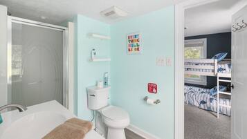 A bathroom with a bathtub, toilet, and shower. There is a shelf with toiletries and a sign on the wall.