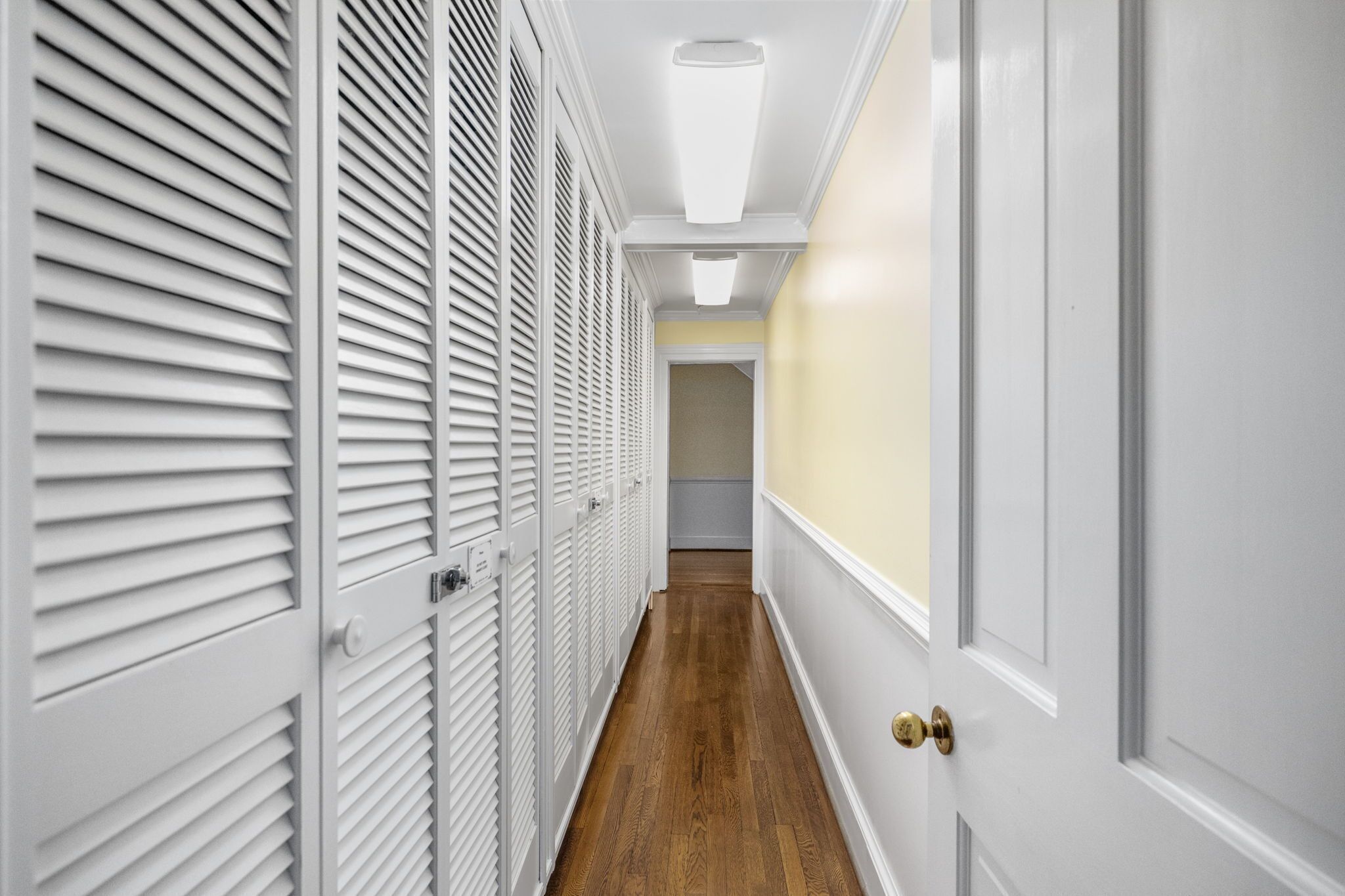 Un couloir avec des placards à persiennes blanches et un plancher en bois.