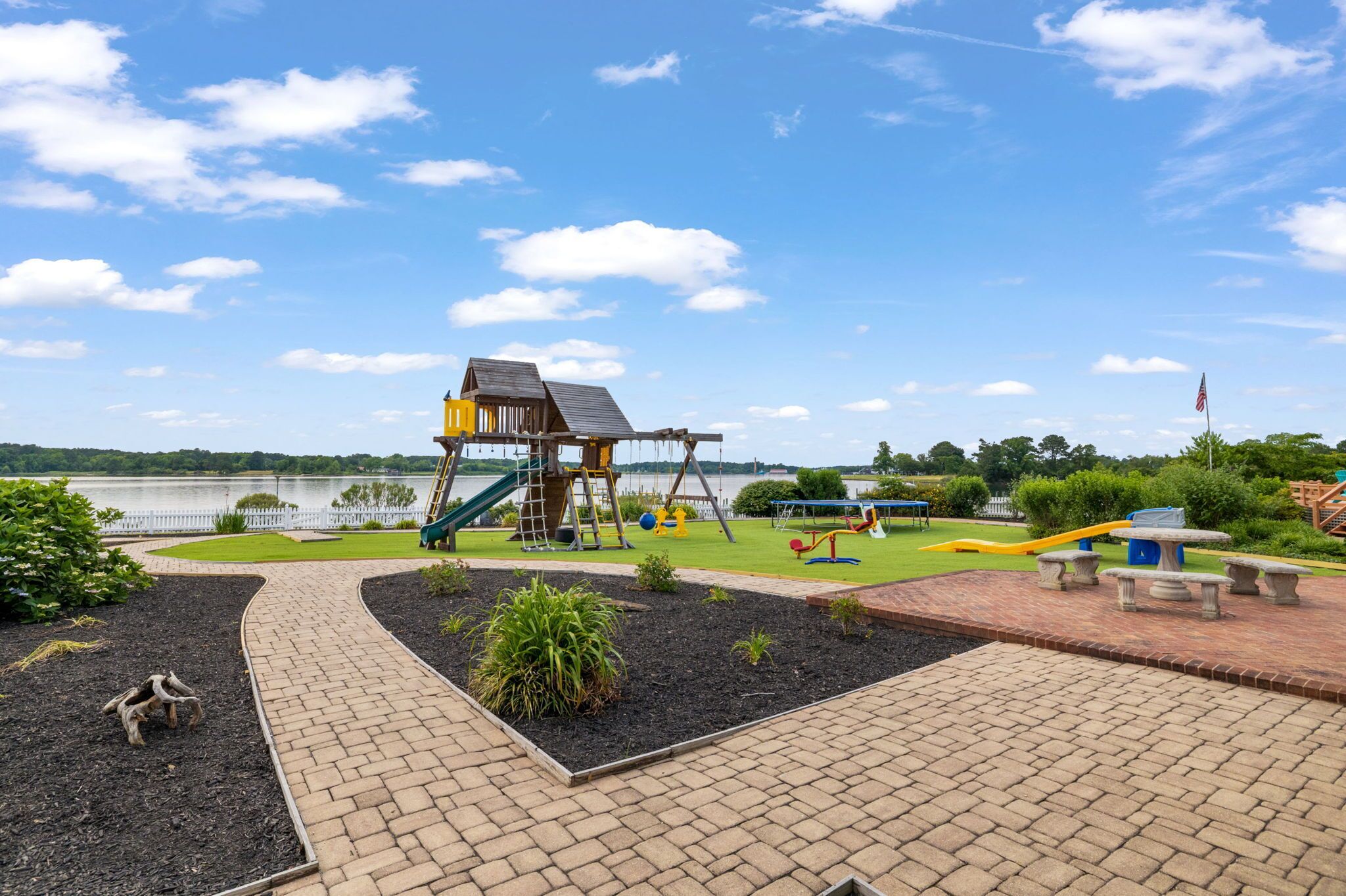 Un parque infantil con columpios, tobogán y estructura para escalar cerca de un lago.